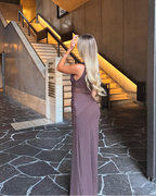 Woman in a long dress standing in a modern interior setting with a staircase.