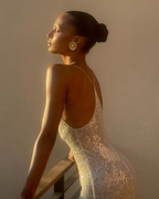 A woman wearing a sparkling champagne-colored sleeveless dress, photographed in a warm indoor setting. The photo is shown within a social media interface screen labeled 'Saved' by the account 'jastookes'.