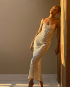 A woman wearing a sleeveless, fitted champagne-gold sequined dress posing in a sunlit indoor setting. The photo appears to be from a social media post, with the caption text partially visible and a large gray overlay obscuring the center.